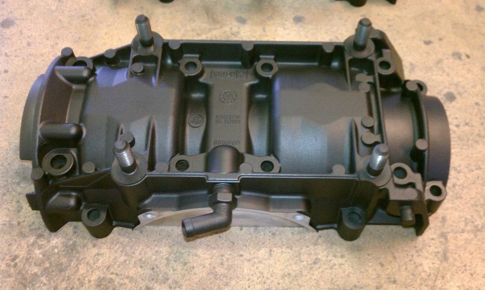 Black engine block with bolts protruding, on a gray surface.