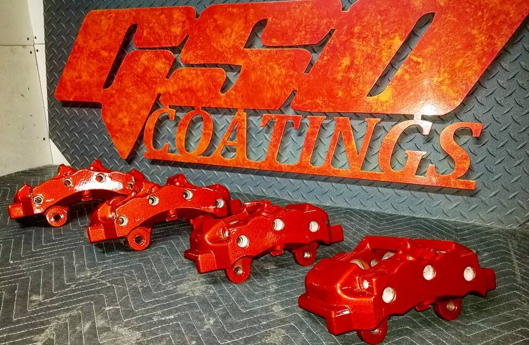 Two gold-colored brake calipers in front of a black wheel and tire, sitting on a textured surface.