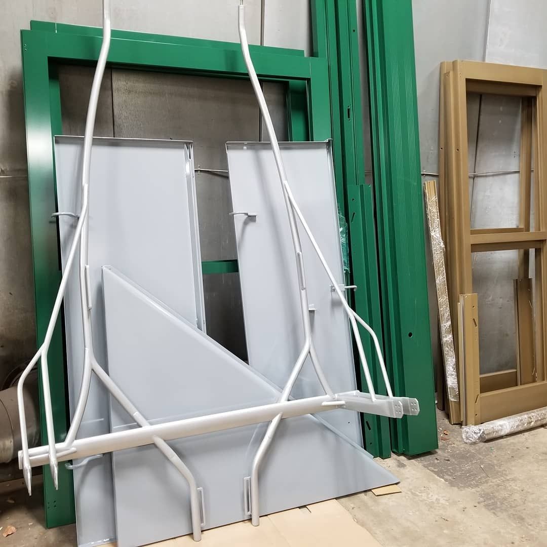 Metal frame with gray panels, green window frames, and a wooden window frame against a wall.