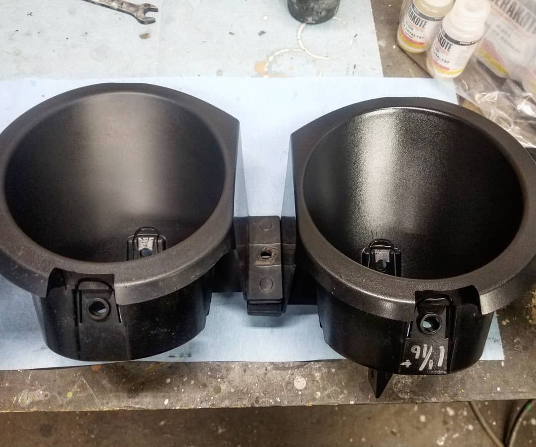Two black, round plastic cup holders attached together, likely automotive.