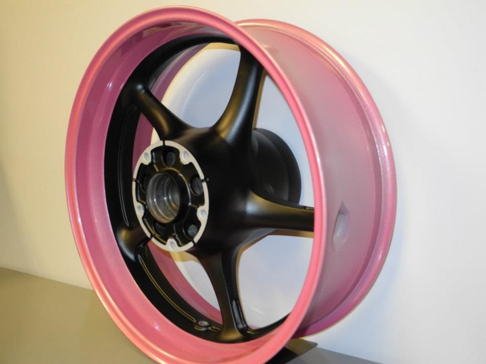 Pink and black motorcycle wheel against a white wall.