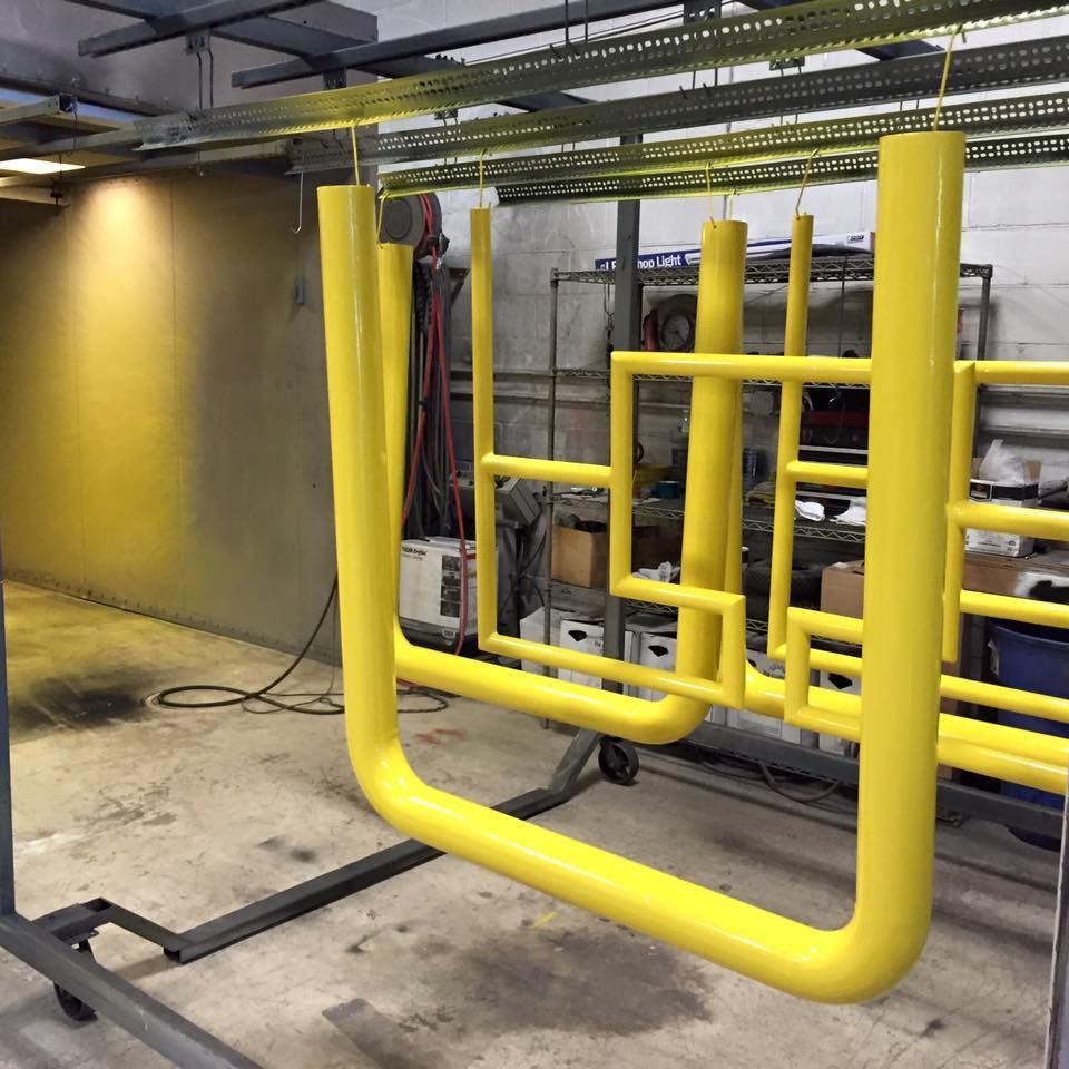 Yellow metal safety barriers hanging from overhead track in a workshop.
