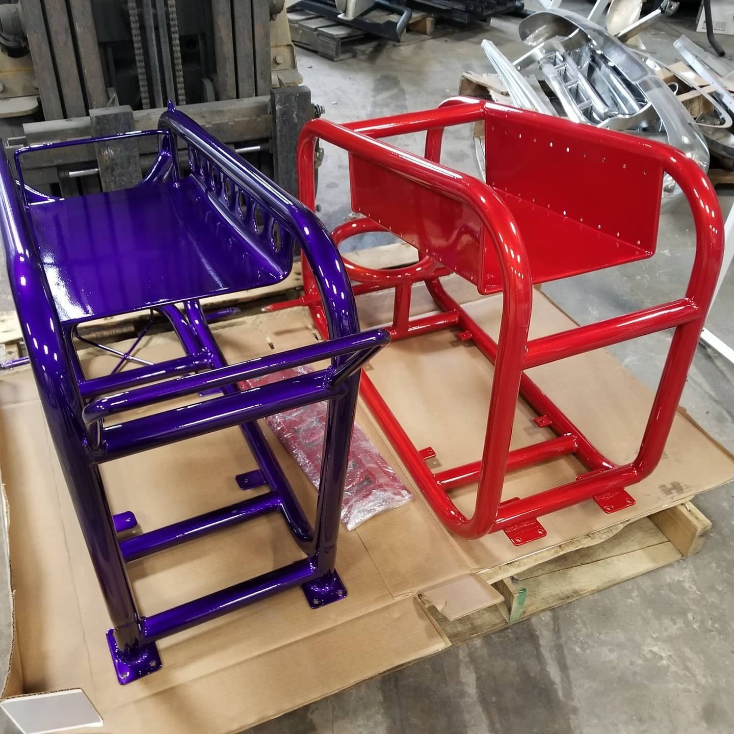 Two metal chassis, one purple, one red, resting on a pallet.