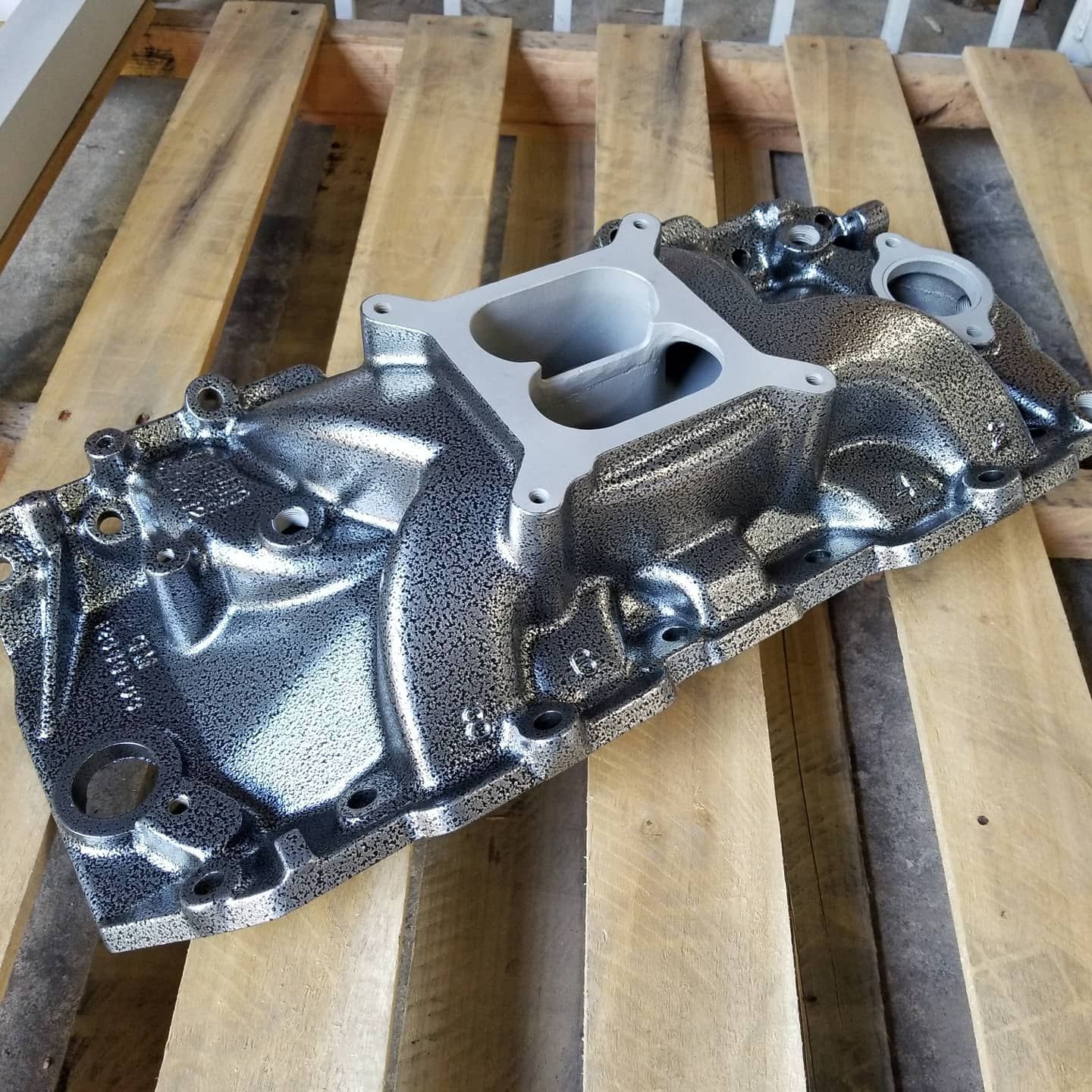Black and silver engine intake manifold on a wooden pallet.
