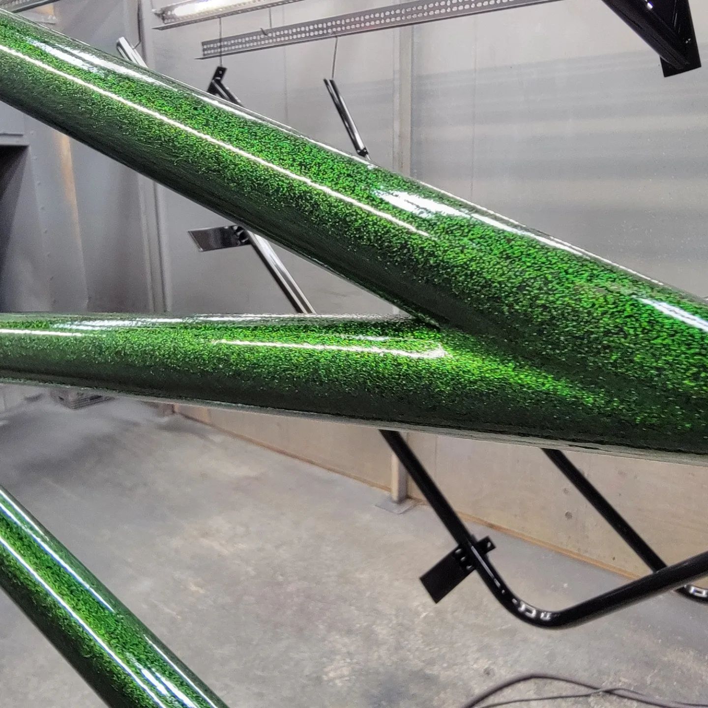 Green glitter-painted boat frame parts hanging in a workshop, supported by black stands.