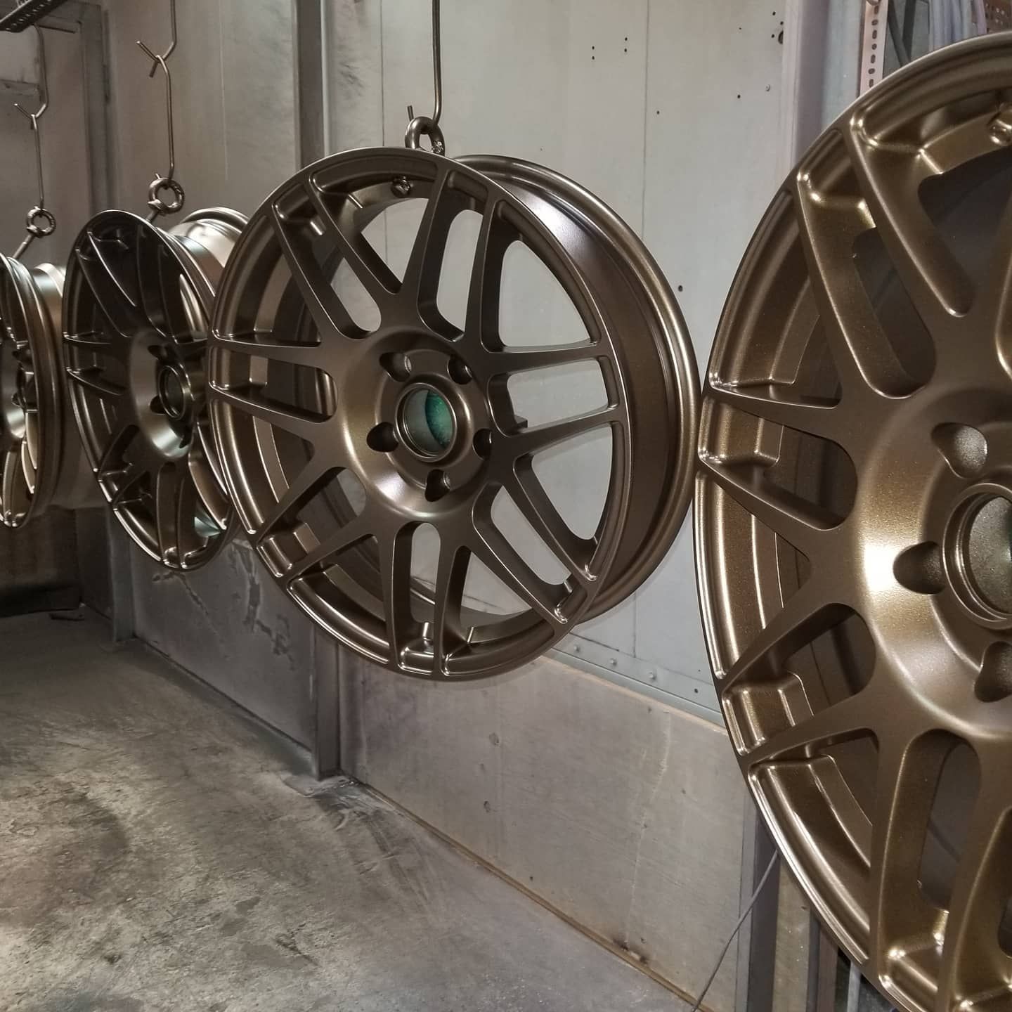Four bronze-colored car rims hanging in a workshop, ready for painting.