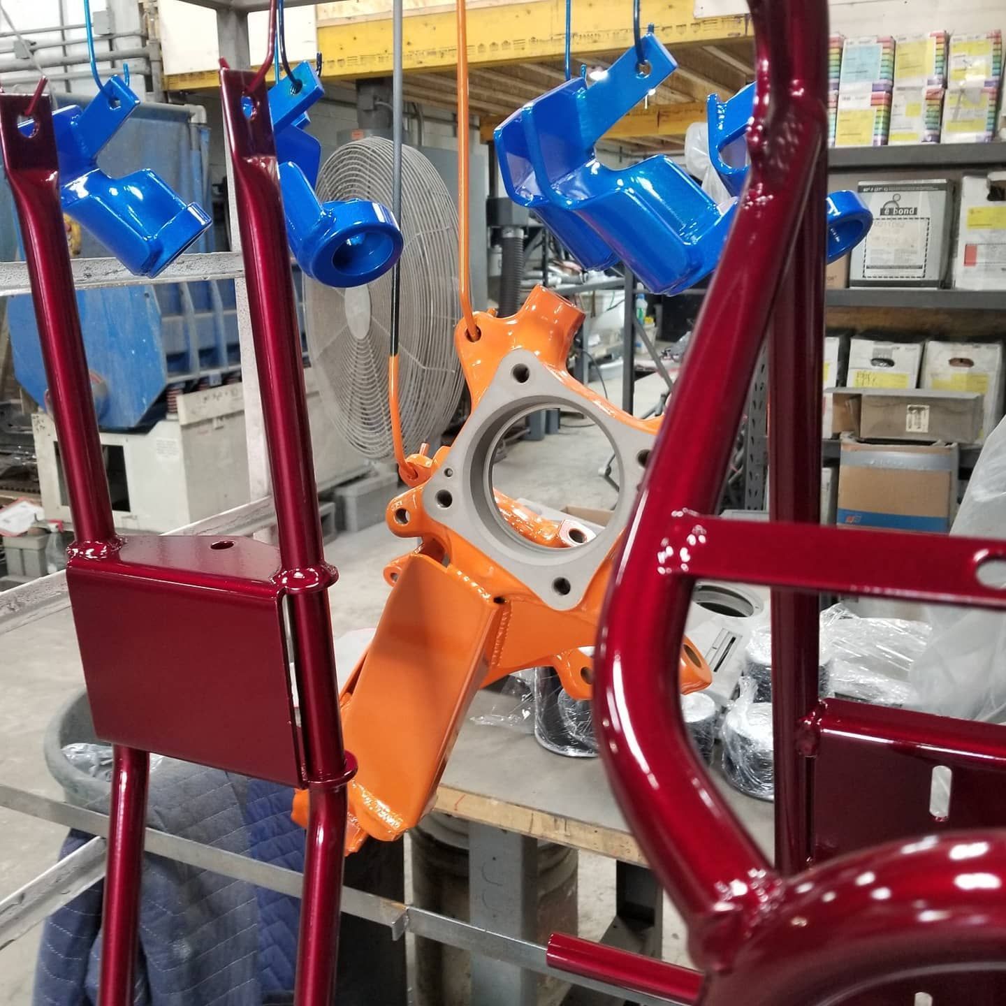 Metal parts in various colors hang in a workshop; orange, red, and blue components.