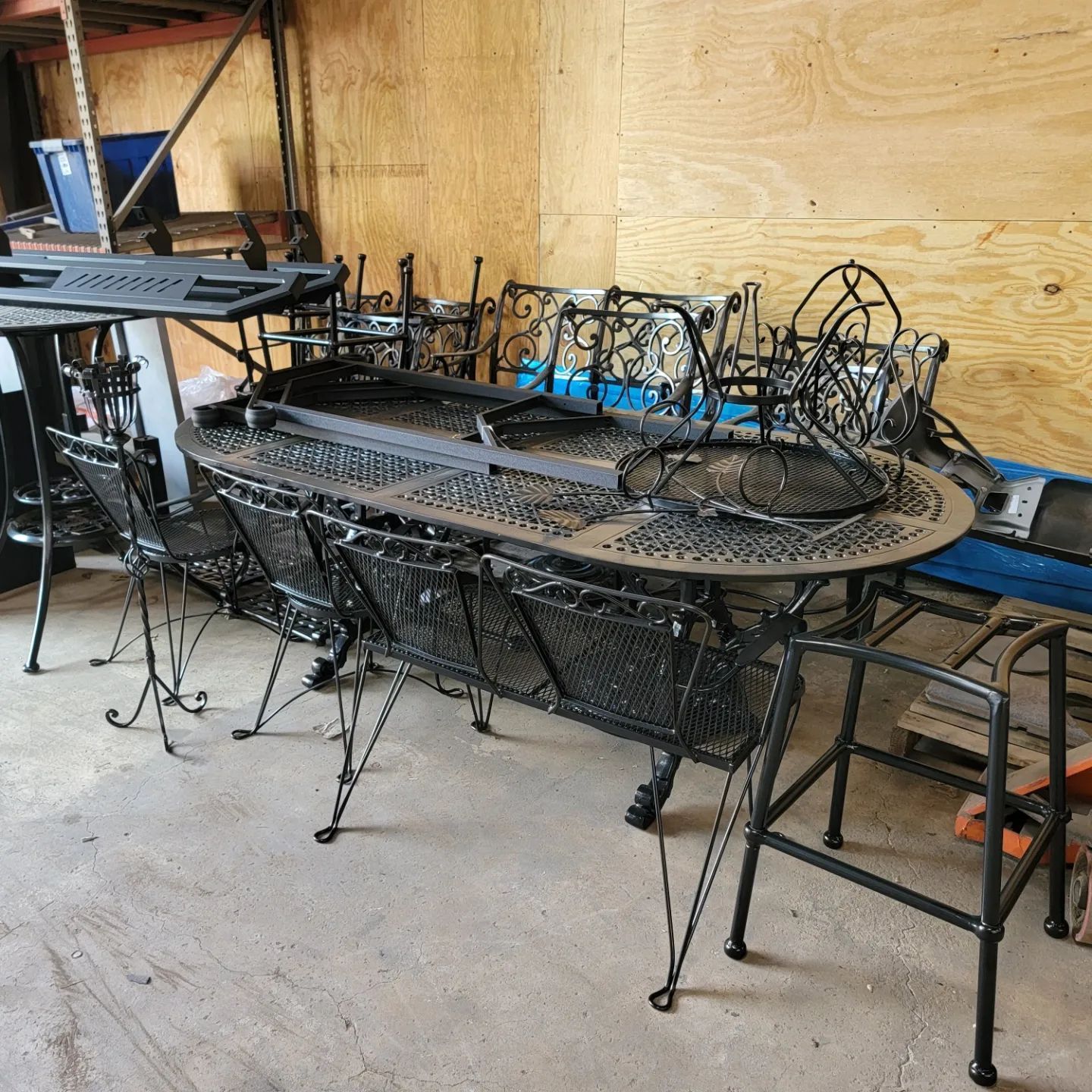 Black wrought-iron patio furniture, including a table and chairs, in a workshop.