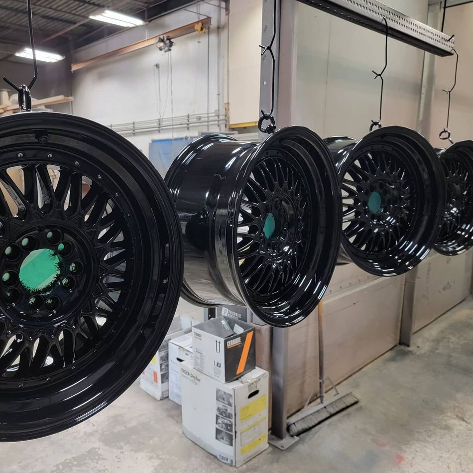 Black car rims, newly painted, hanging in a workshop setting.
