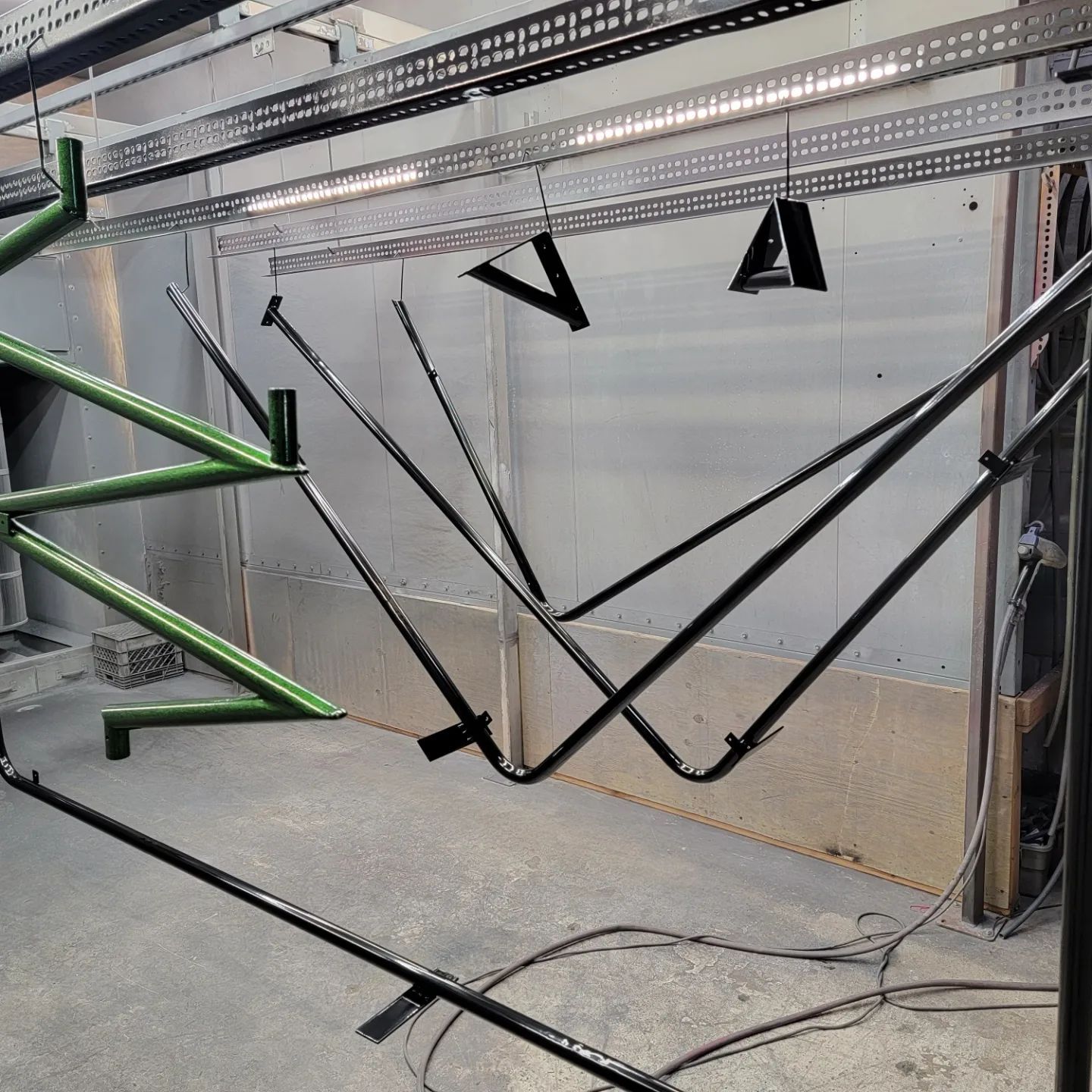 Metal frames hanging inside a spray painting booth; some are green, others are black.
