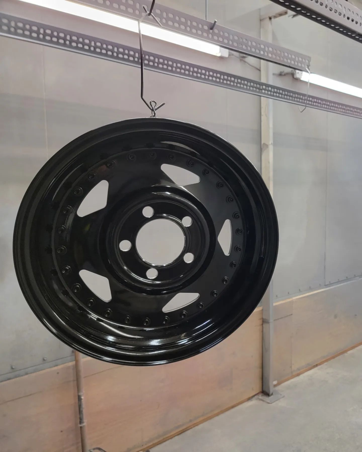 Black car wheel suspended in a spray booth, ready for painting.