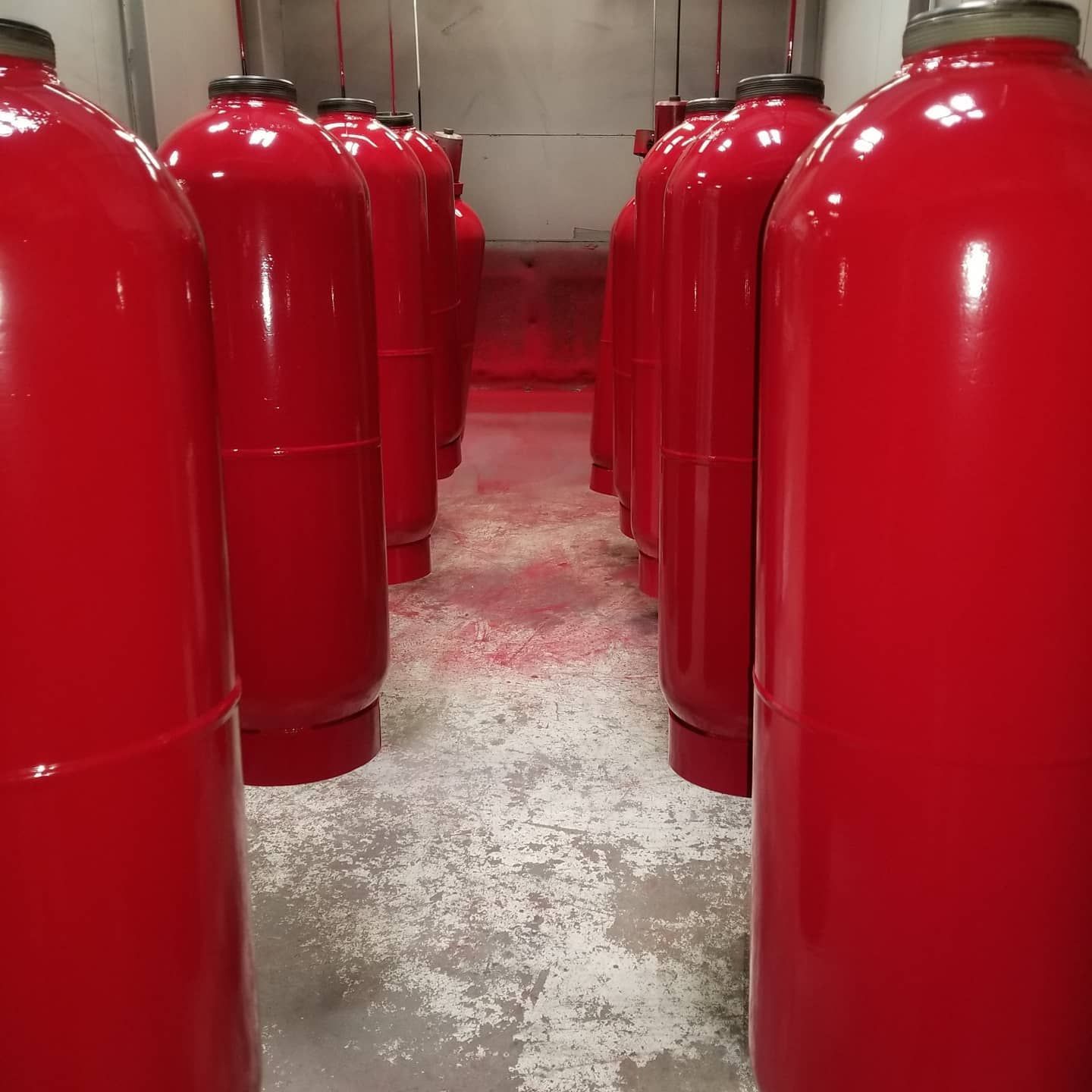 Red metal cylinders in a row, likely freshly painted, inside a workshop.