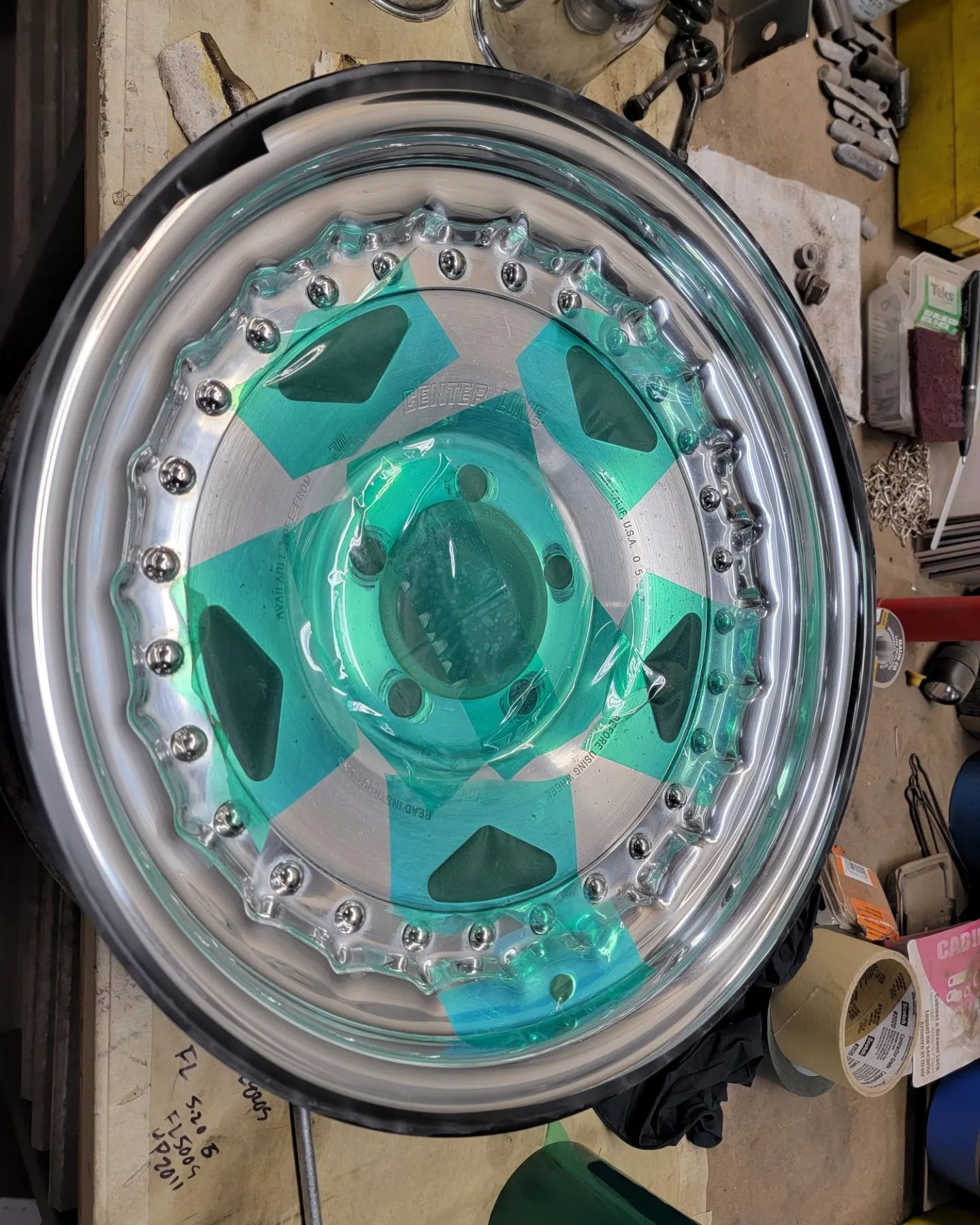 Chrome car wheel with turquoise and silver accents, partially taped off.