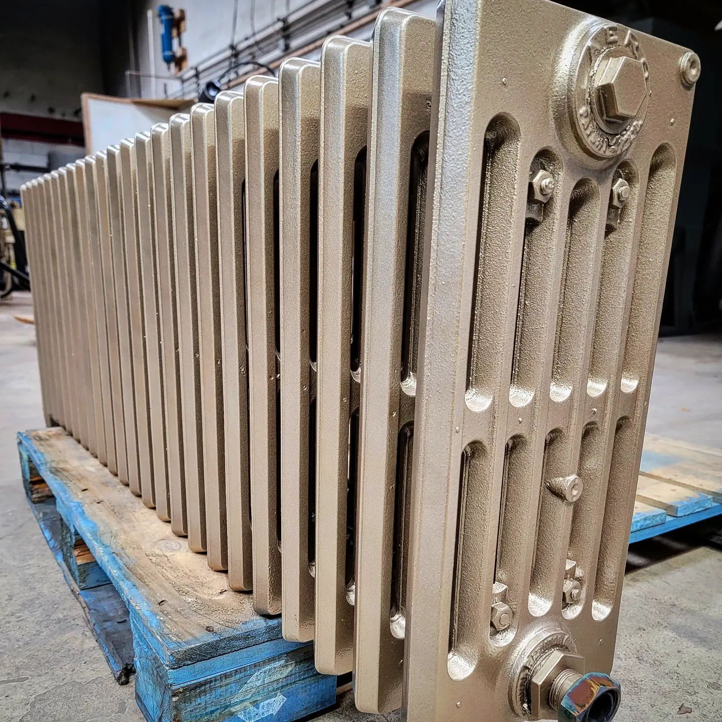 Large, gold-painted cast iron radiator on a blue wooden pallet in an industrial setting.
