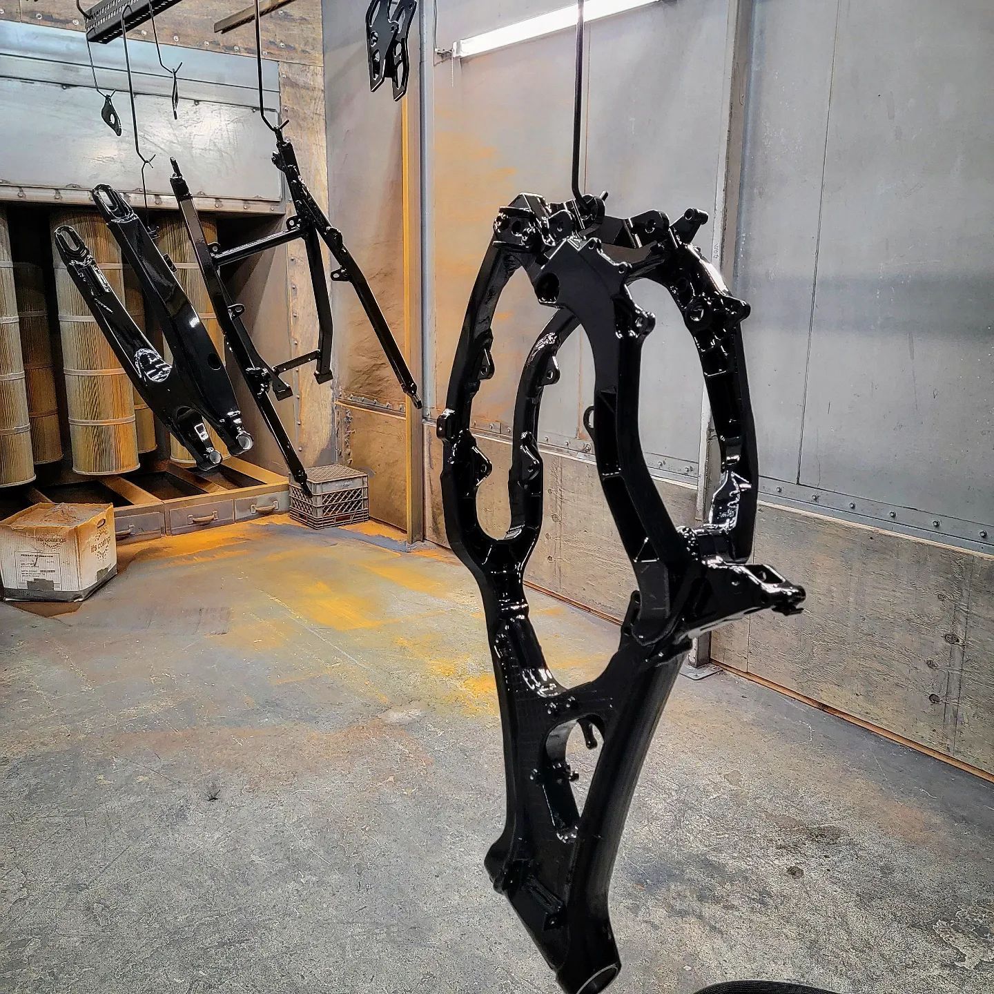 Black metal frames hanging in a spray painting booth.