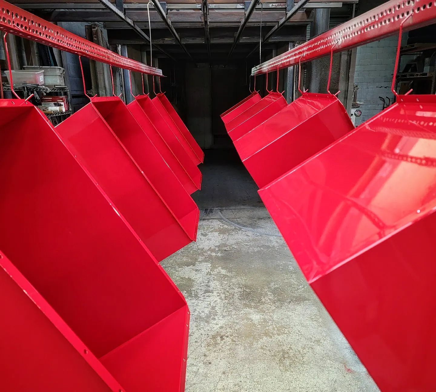 Red metal bins hanging from an overhead rail system in a workshop.