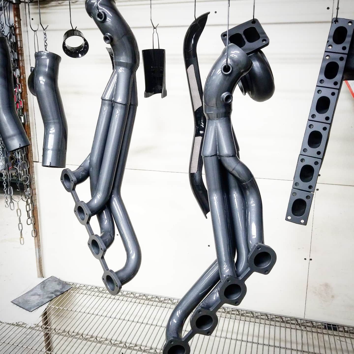 Gray exhaust headers and components hanging to dry after coating.