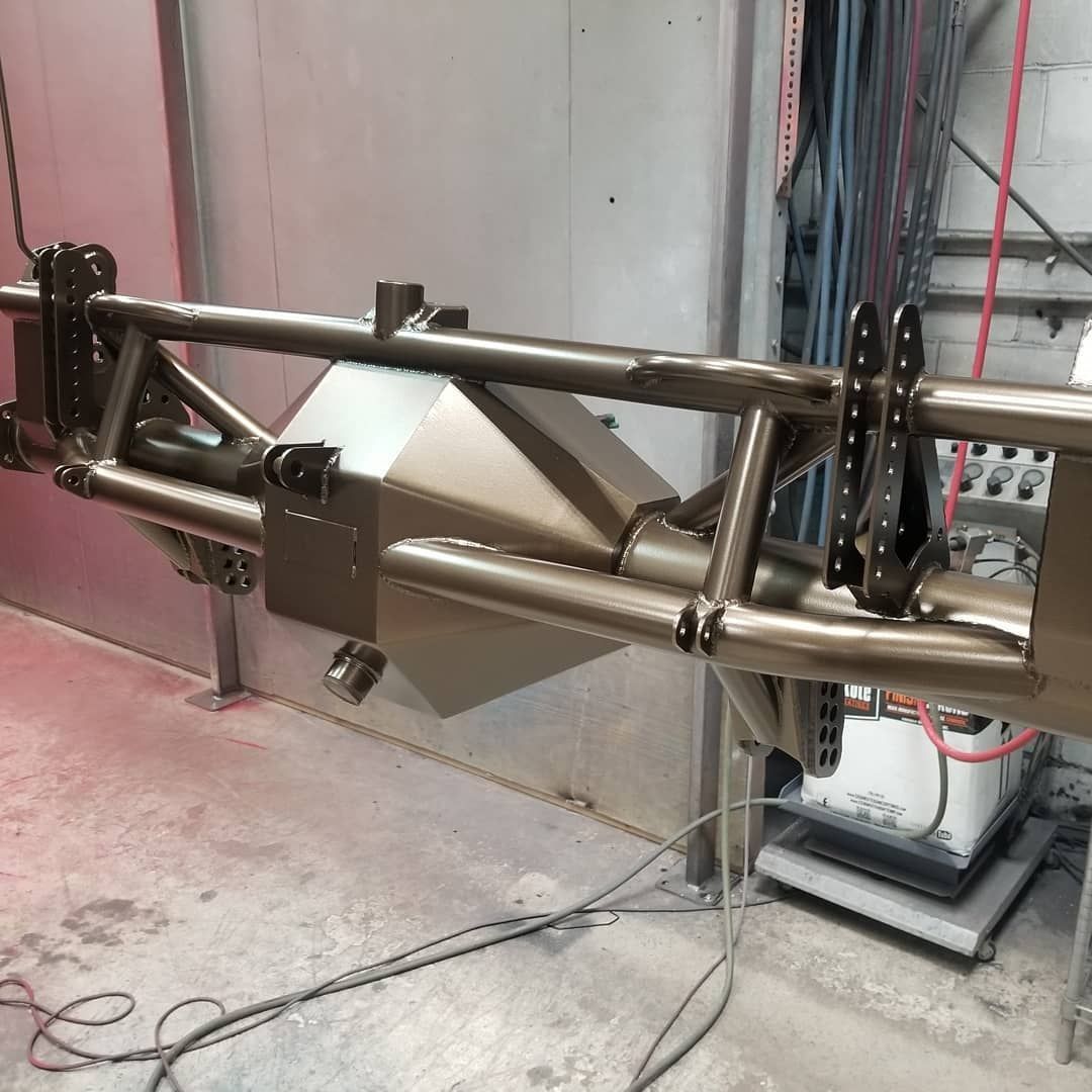 Metal framework, likely for a vehicle, is painted tan in a workshop environment.