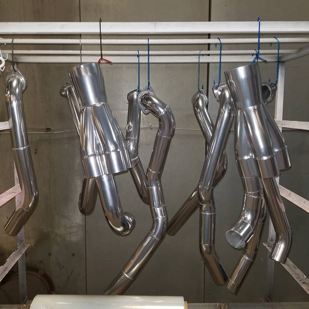Exhaust manifolds hanging inside a spray booth. Shiny metal parts suspended by blue wires.