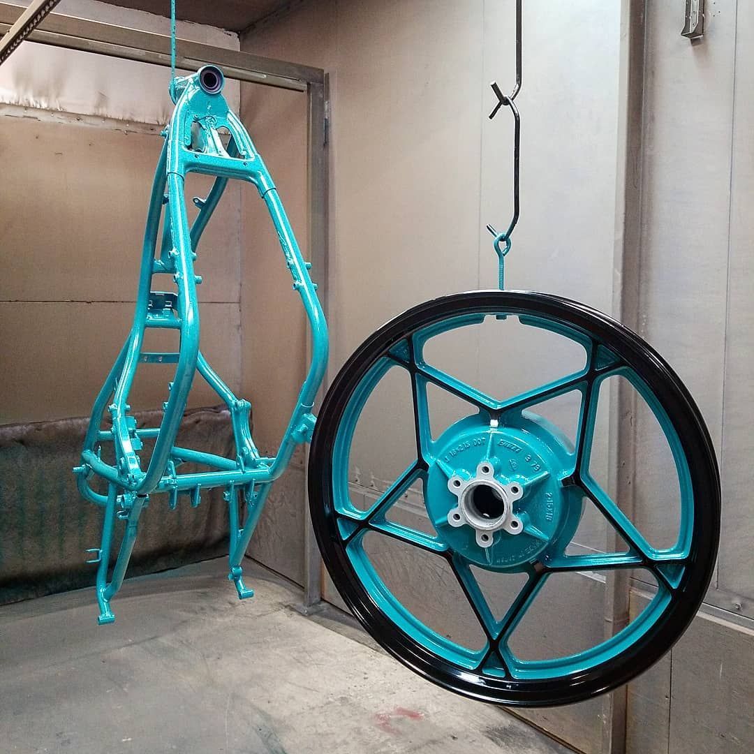 Blue motorcycle frame and wheel, freshly painted, hanging in a spray booth.