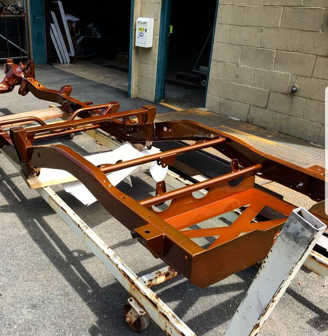 Bronze-painted vehicle chassis on a wheeled cart, in front of a brick building.