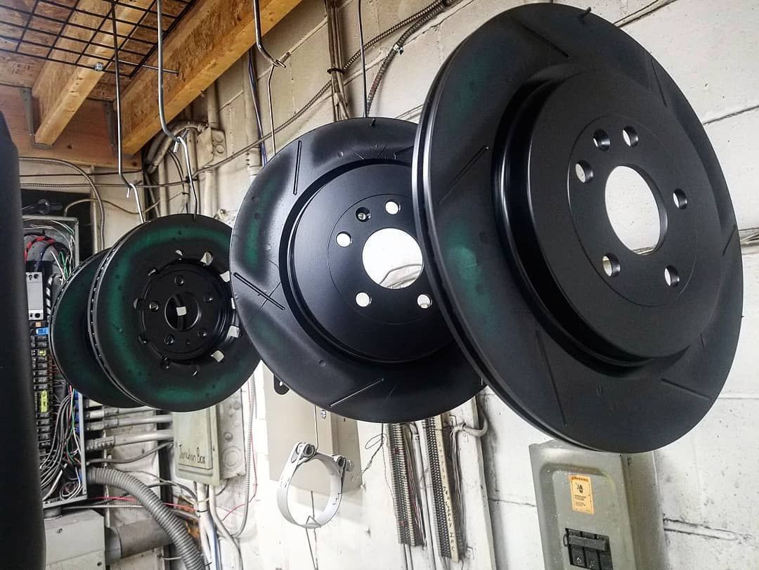 Four black brake rotors hanging on hooks; workshop setting.