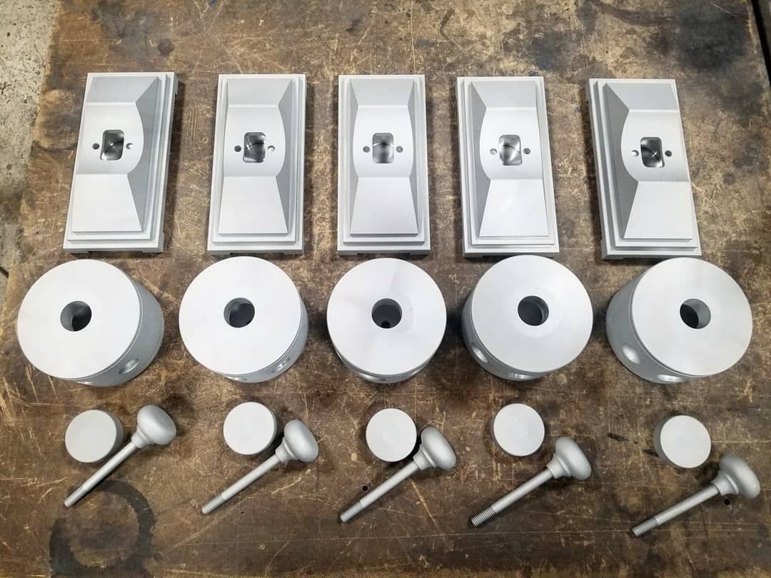 Five sets of machined metal components laid out on a surface: bases, tops, and handles.