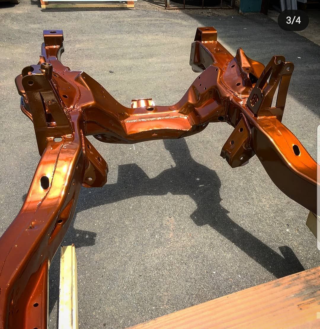 Orange painted car frame, resting on wood blocks outdoors.