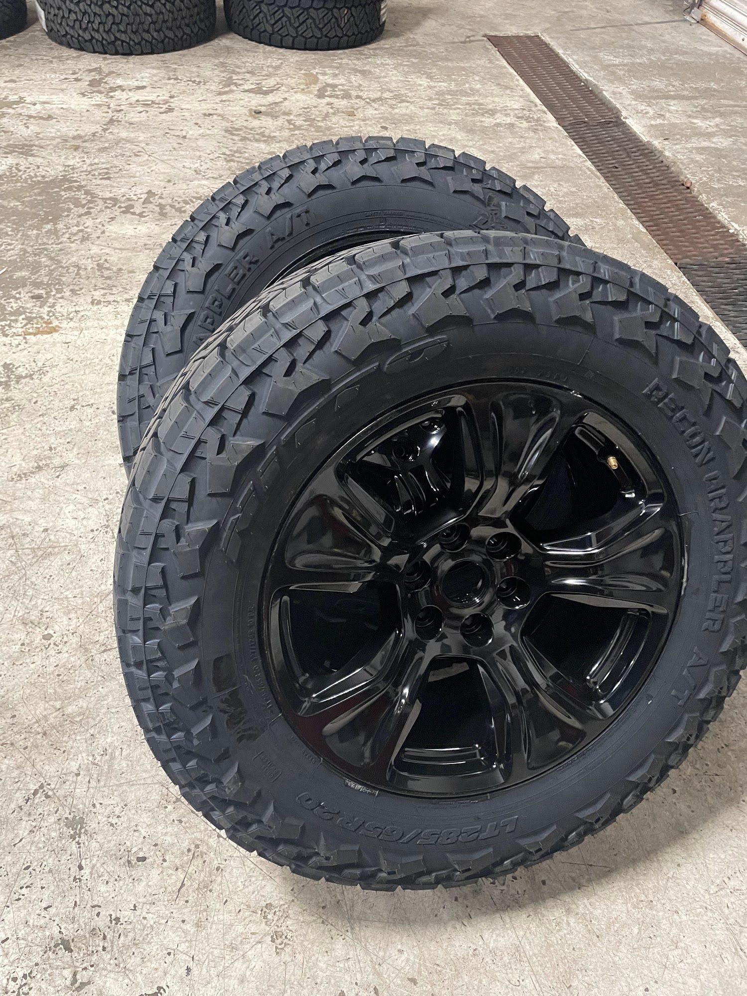 Two black alloy wheels with off-road tires, set against a concrete floor.