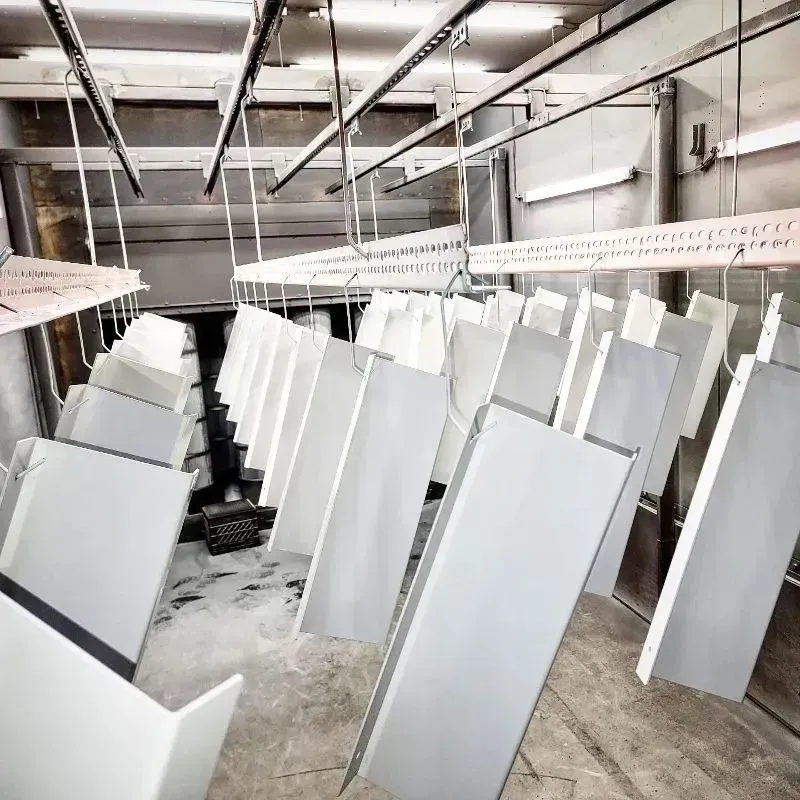White painted metal panels hanging from an overhead conveyor system in a factory.
