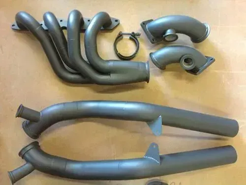 Gray automotive exhaust system components laid out on a surface, including headers, tubes, and a clamp.