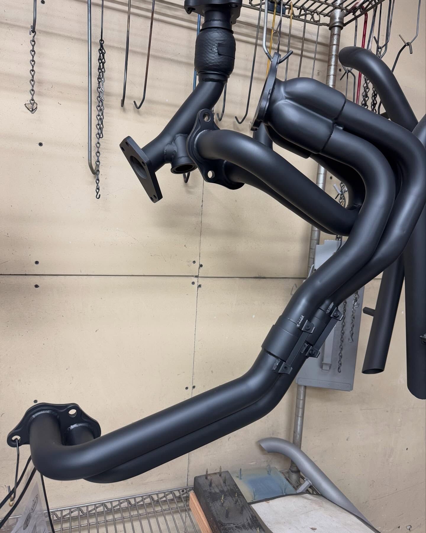 Black exhaust headers hanging in a workshop.
