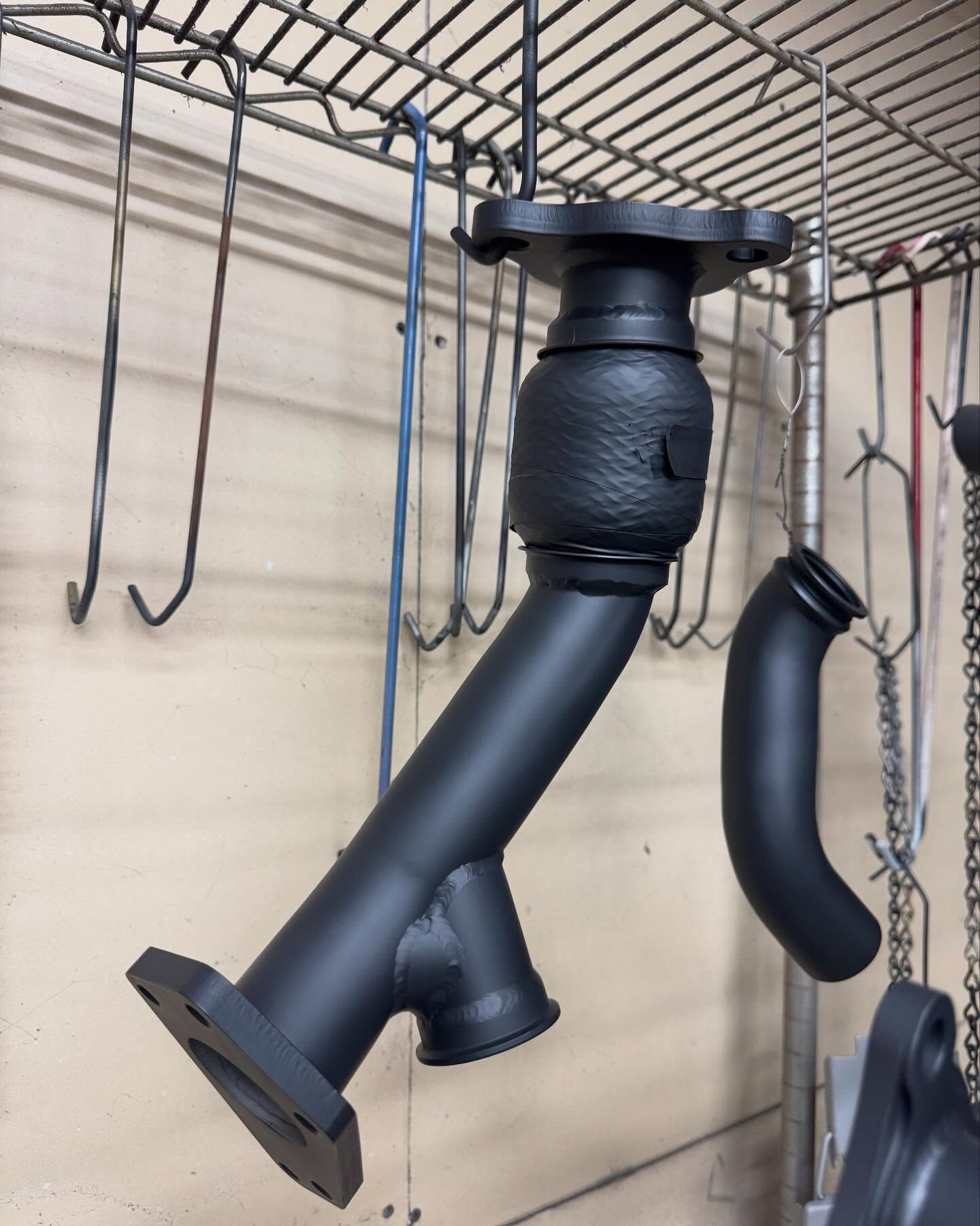 Black exhaust manifold hanging on a rack, freshly painted.