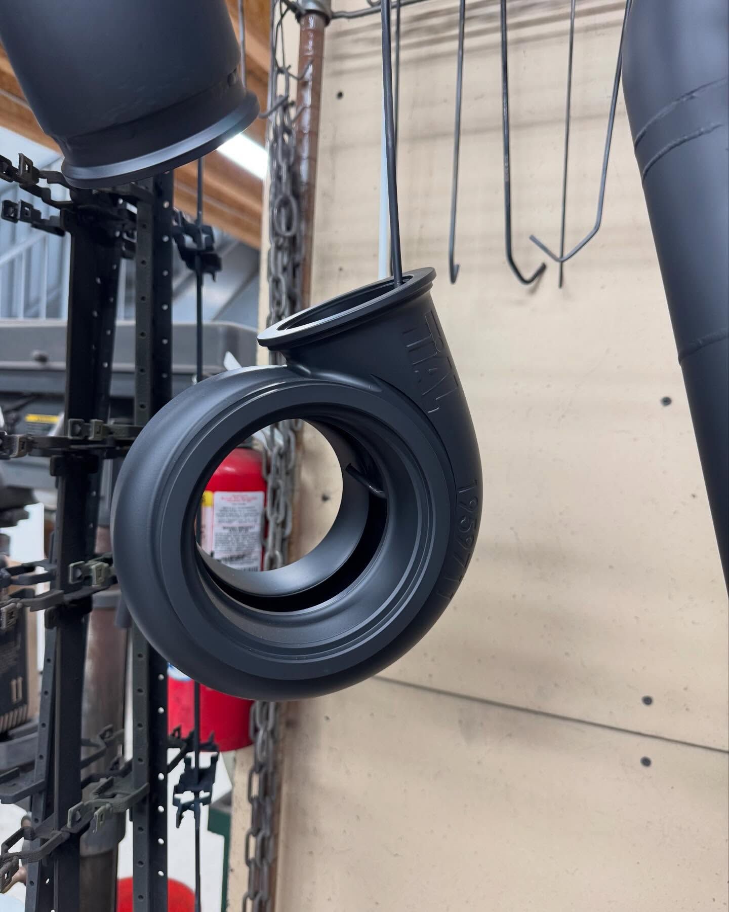 Black, circular metal part, likely for machinery, hanging on a rack after coating.