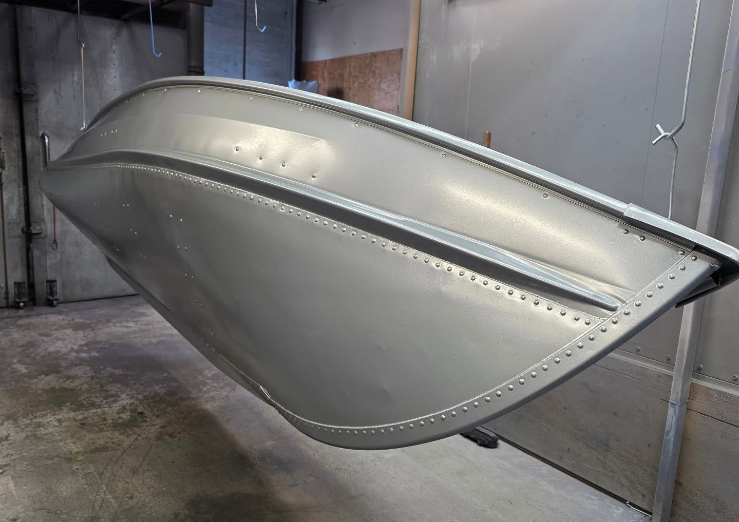 Aluminum boat hull, freshly painted silver, suspended in a workshop.