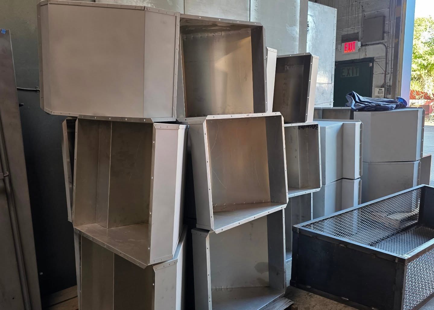 Stack of rectangular metal ductwork sections in a factory setting.