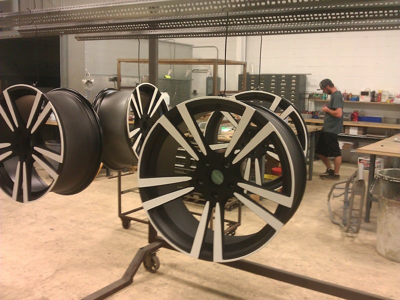 Car wheels, black and white design, on a rack in a workshop, person working in background.