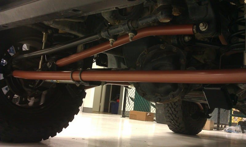 Underside of a vehicle, showing orange-colored suspension components and tires.