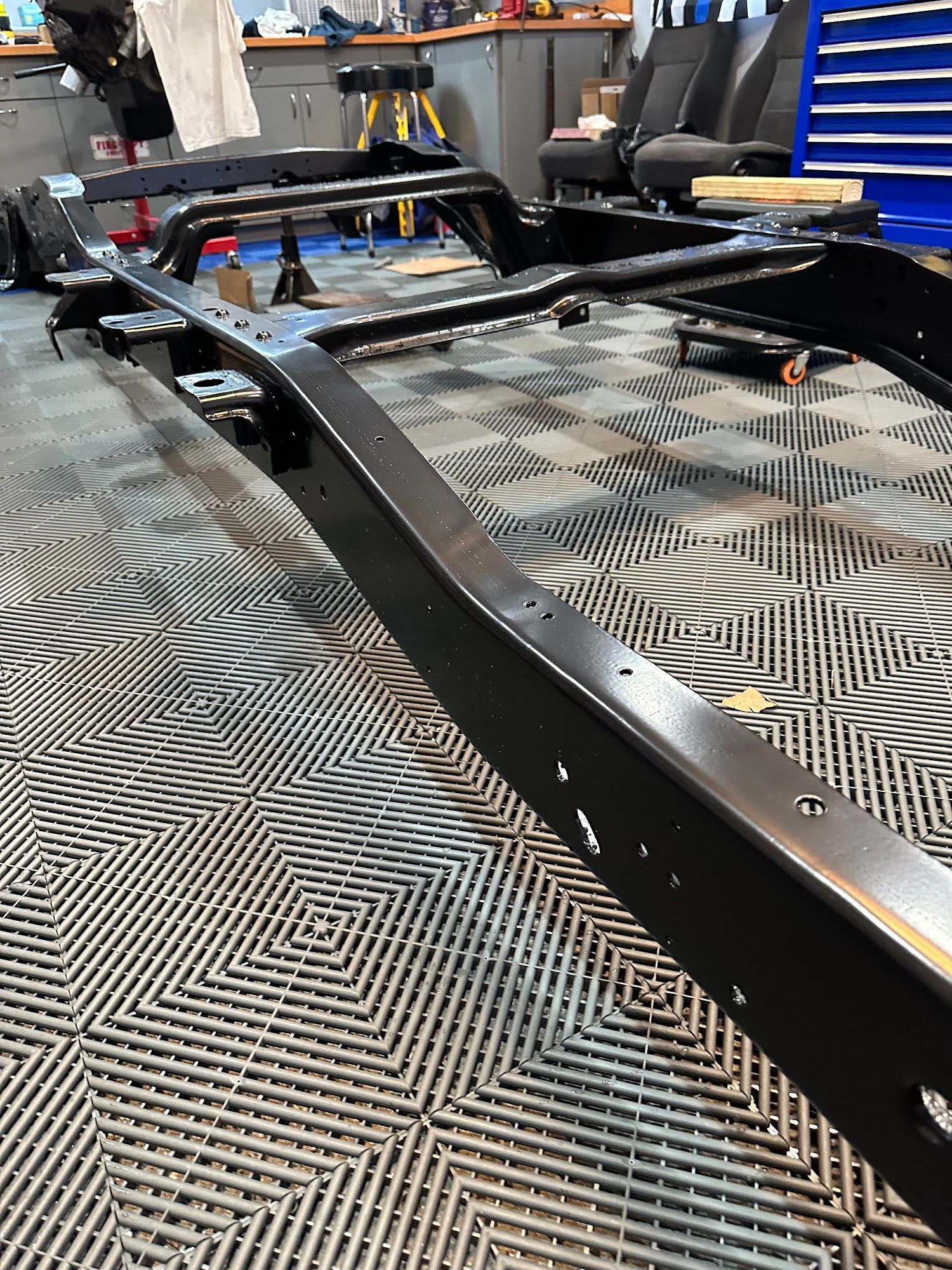 Black vehicle chassis frame on a patterned floor in a garage.