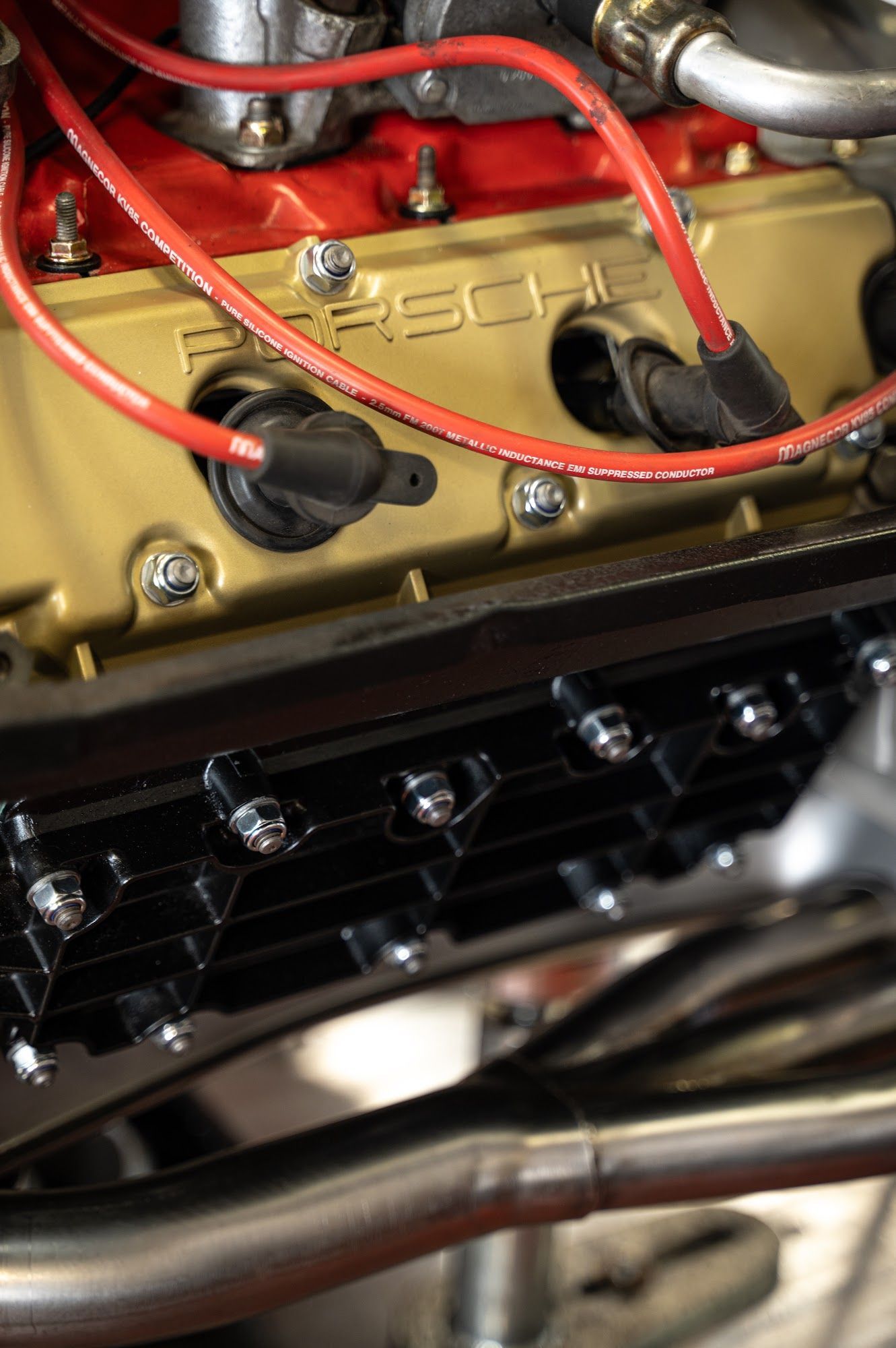 Close-up of a gold Porsche engine with red spark plug wires and a black component below.