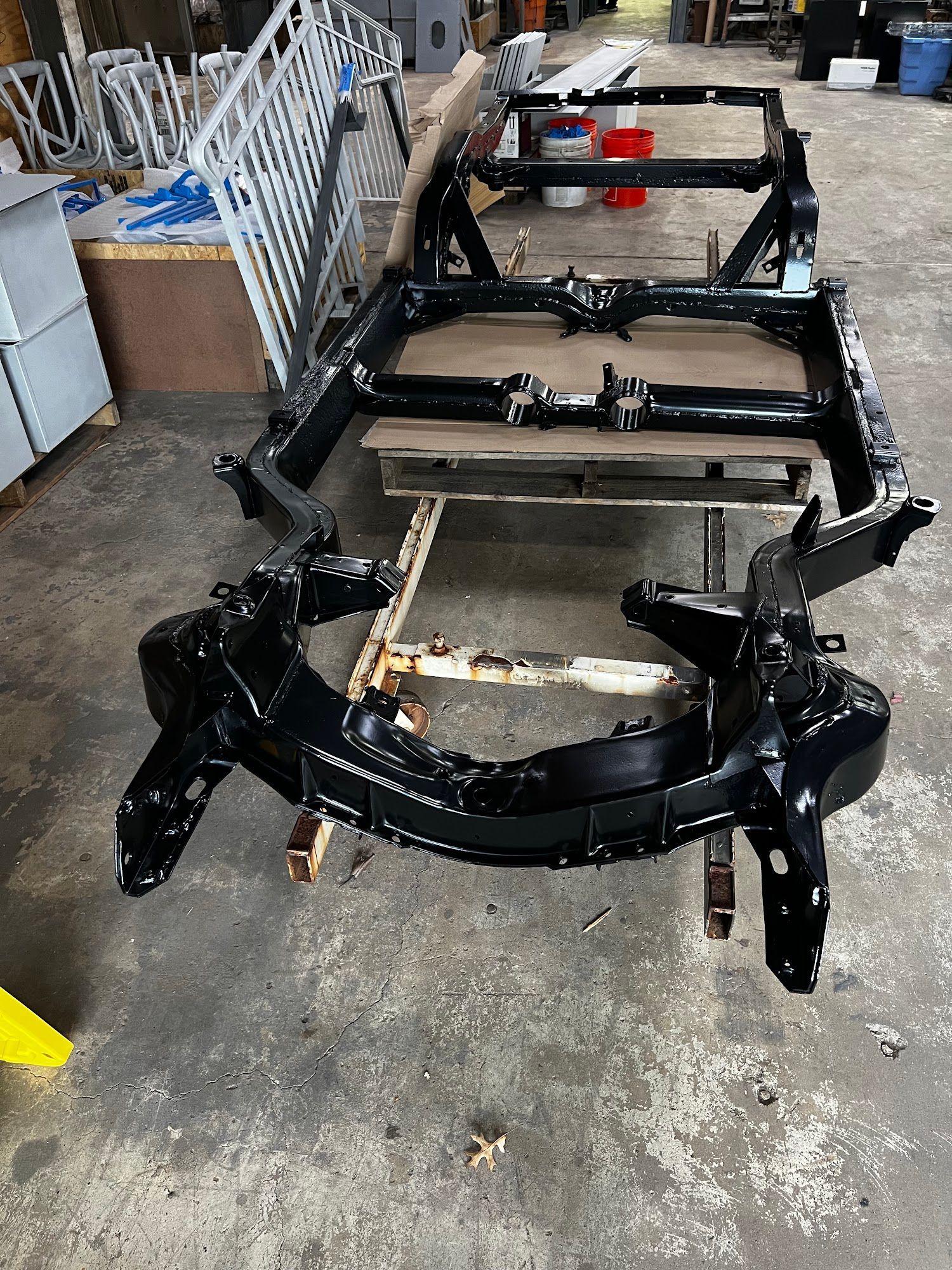 Black painted vehicle frame on a wooden surface in a workshop.