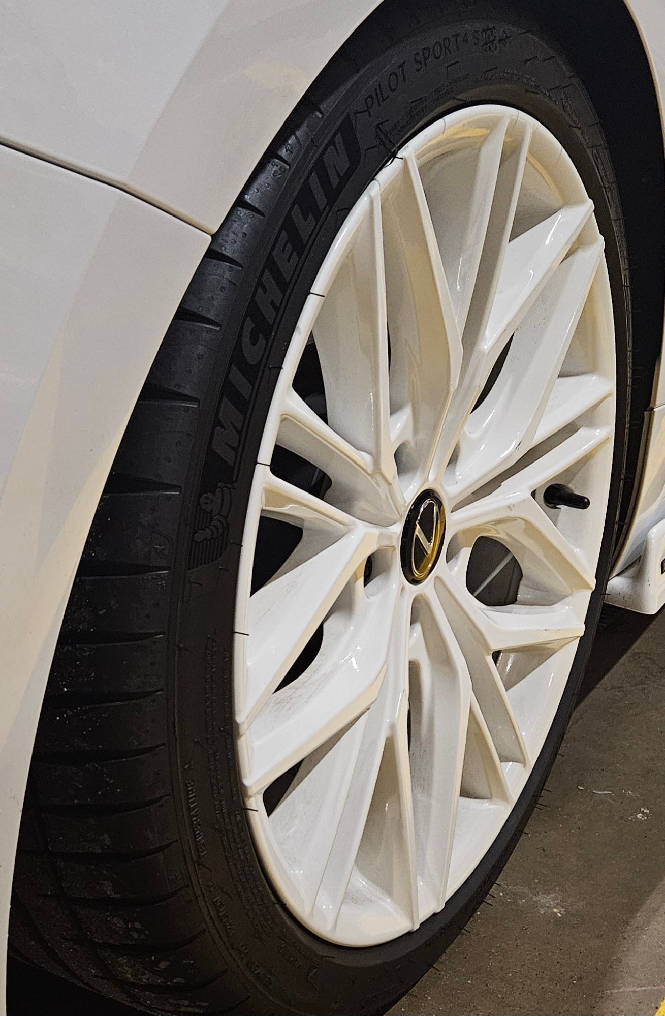 White car wheel with white spokes and a black tire; a VW logo is visible at the center.