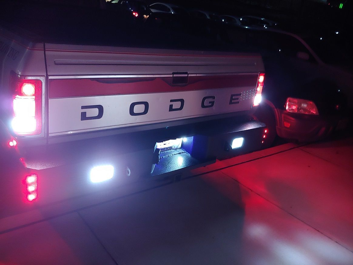 Rear view of a Dodge pickup truck at night with illuminated red and white lights. 