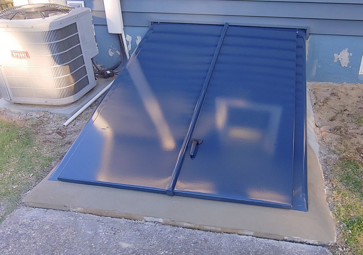 Blue metal cellar doors, hinged, on a concrete foundation, next to an AC unit.