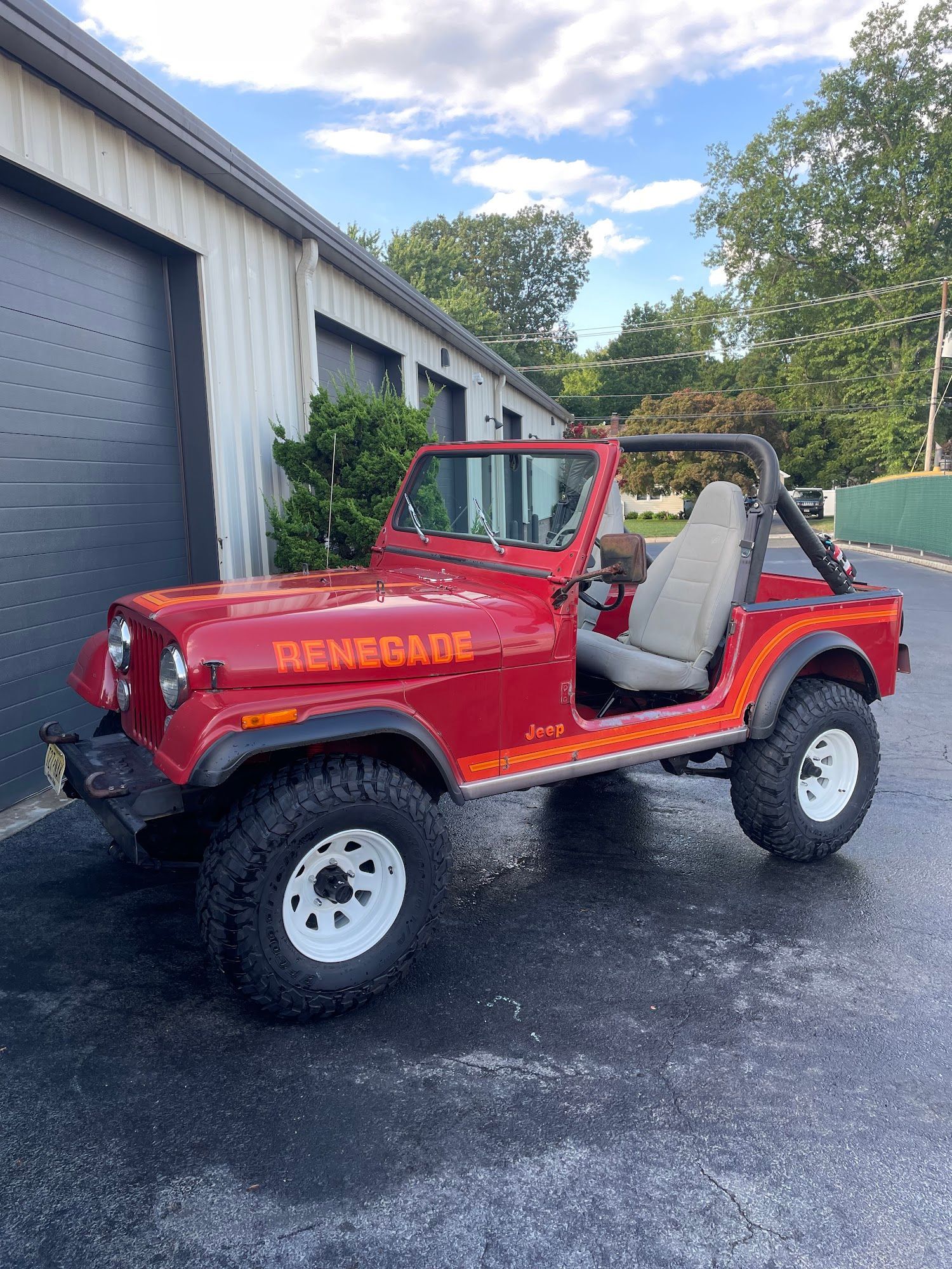 Red Jeep Renegade parked, with white wheels, in front of a building on a paved surface.