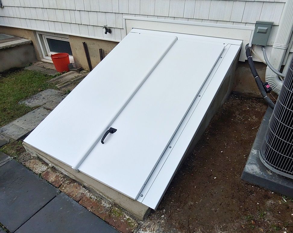White cellar door, partially open. Beside a building, near air conditioner.