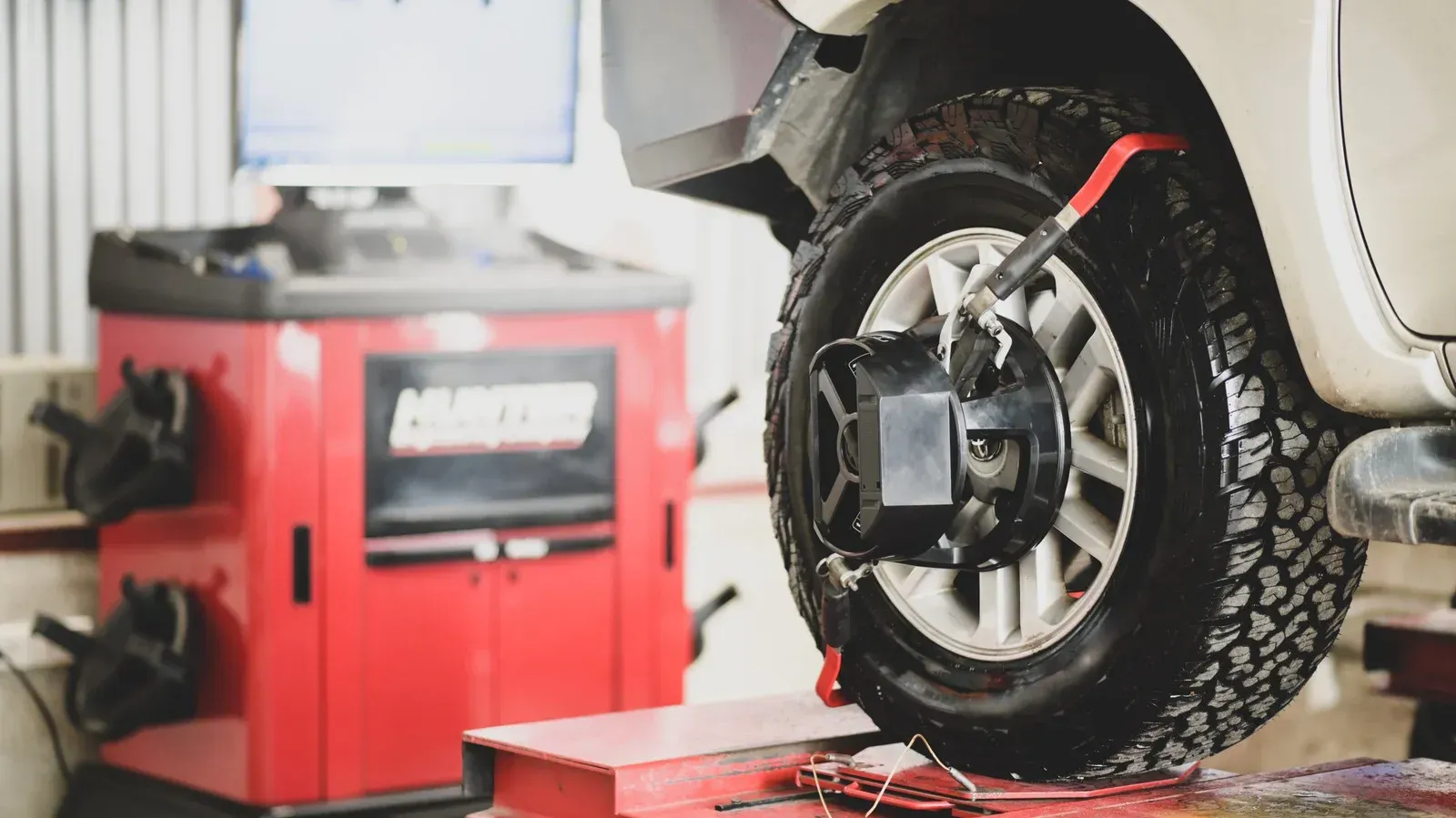 Car tire on a lift, undergoing wheel alignment. Red machine with screen in auto shop.