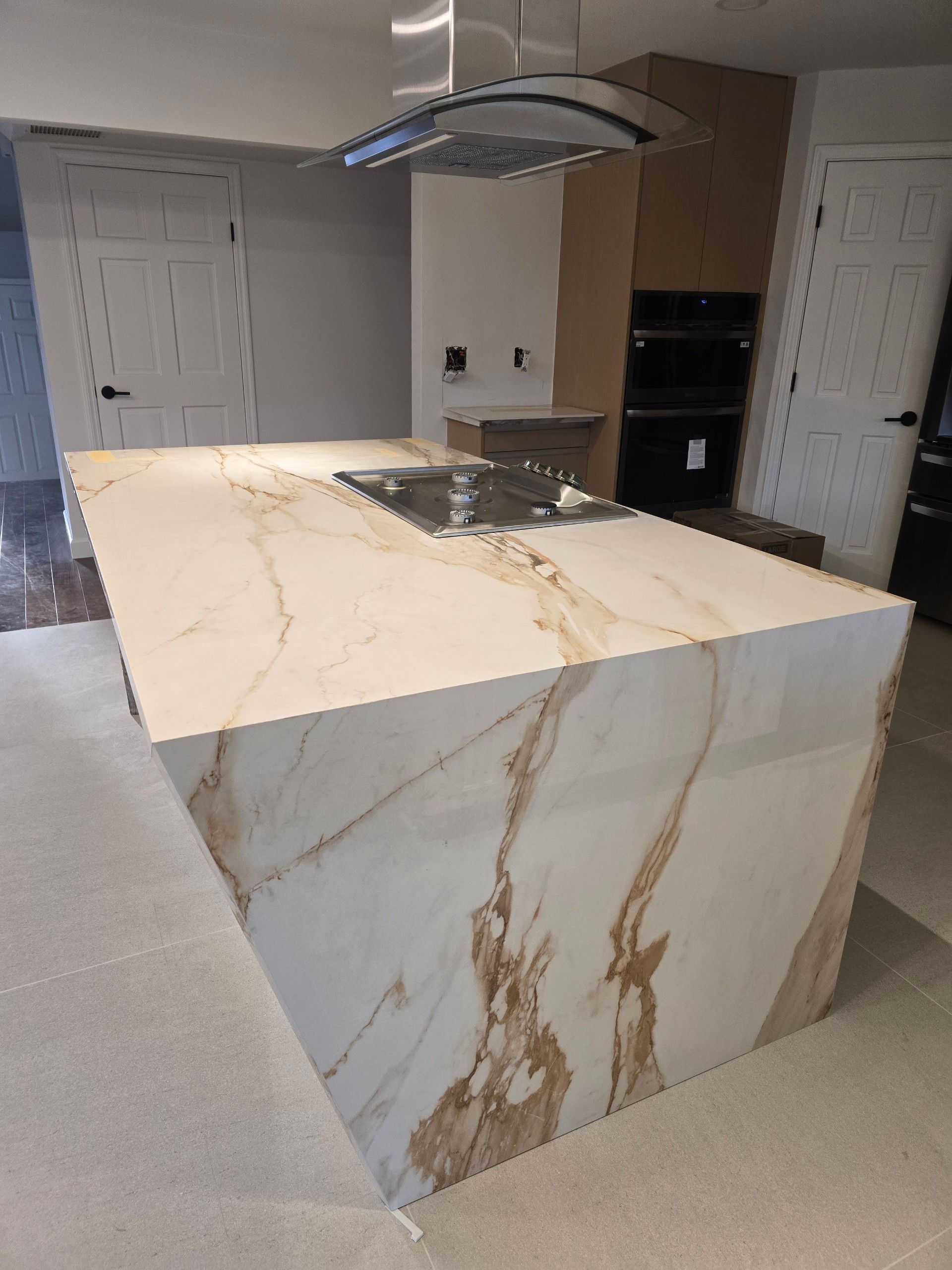Kitchen island with white marble and gold veining, stovetop, modern style.