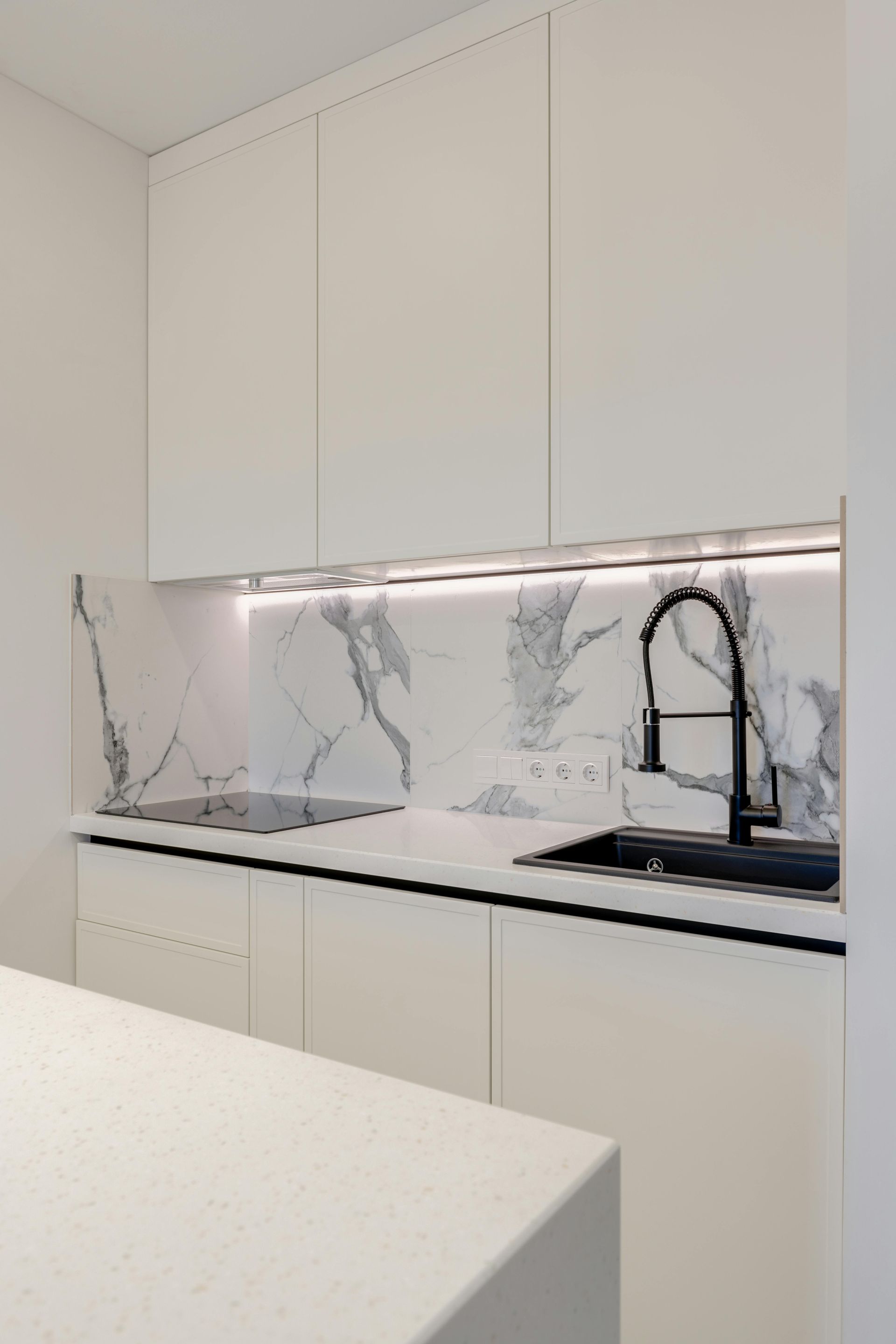 Modern white kitchen with marble backsplash, black faucet, and under-cabinet lighting.