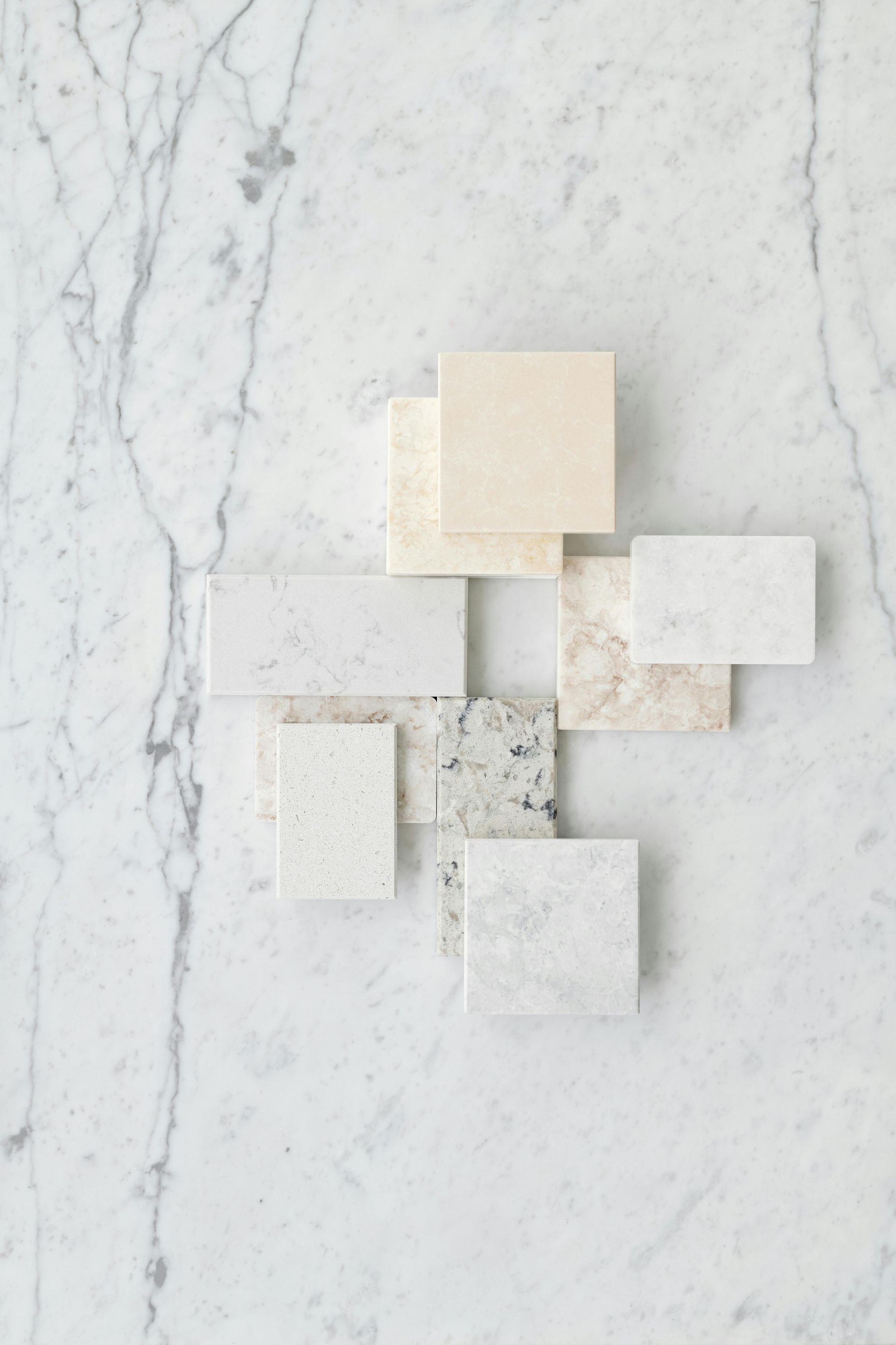 Assortment of white stone tile samples on a marble background, showcasing various textures and colors.